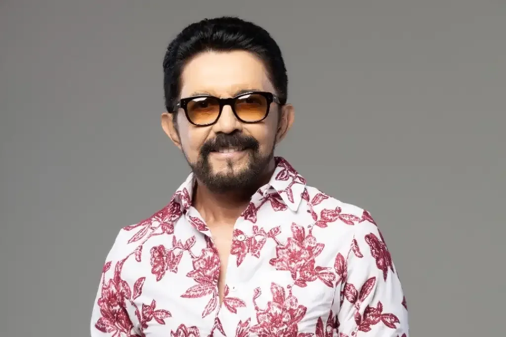 Homem de óculos amarelo e blusa branca com flores vermelhas