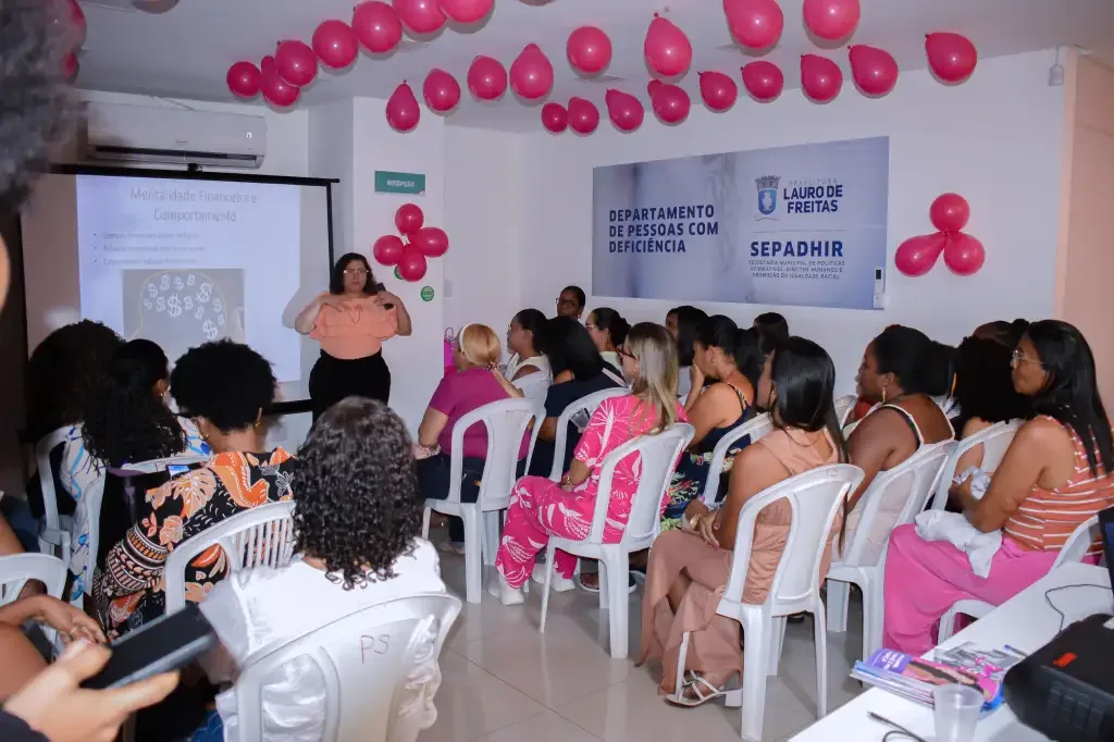mulheres sentadas em cadeiras brancas assistindo um slider e uma mulher falando