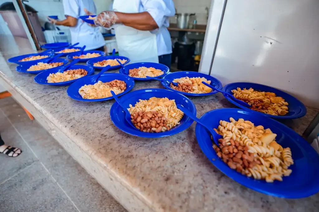 Pratos na cor azul com macarrão e feijão em uma bancada em uma escola