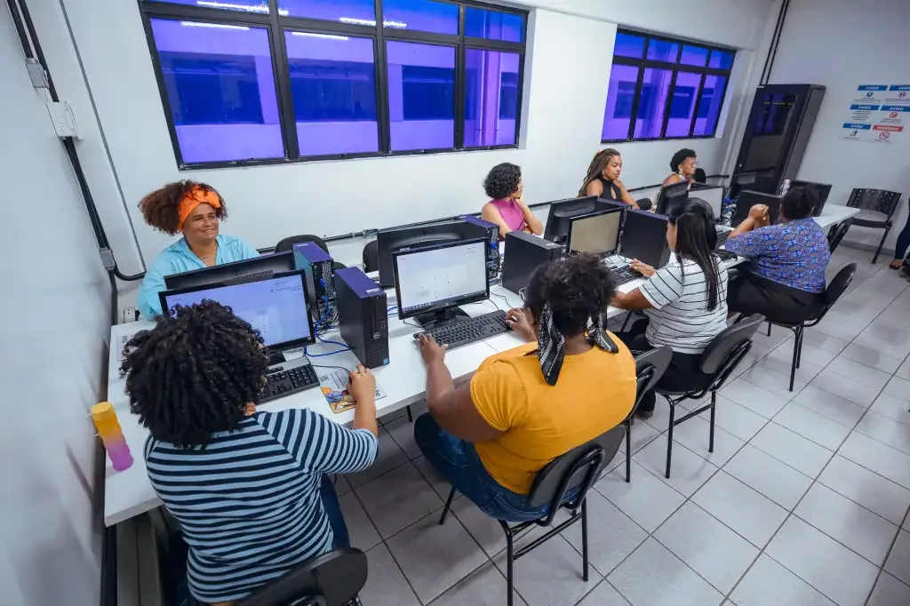 Mulheres sentadas em mesas com computadores para curso de informatica