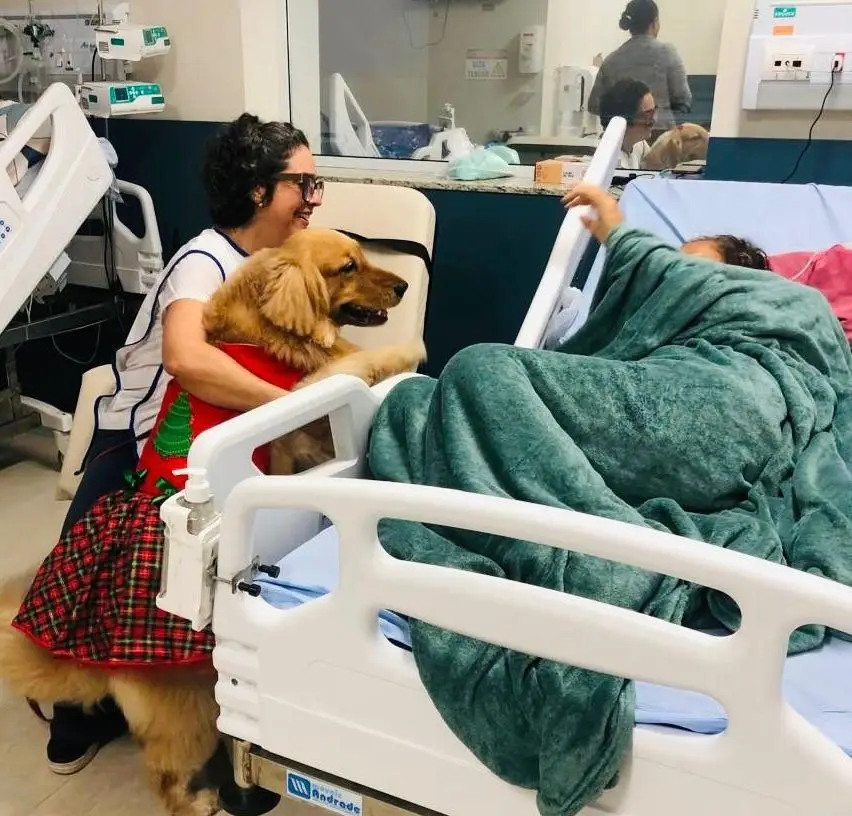 uma tutora com seu cão visitando uma paciente no hospital