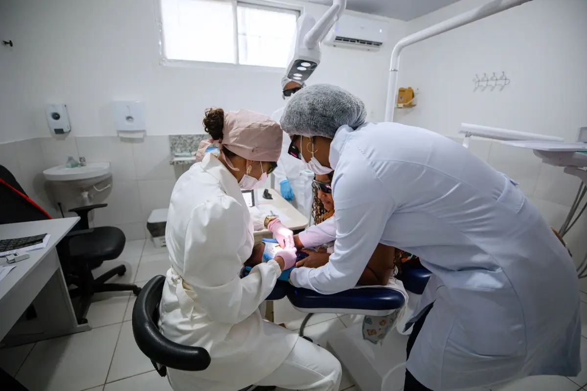 Dentista e auxiliar atendendo paciente.