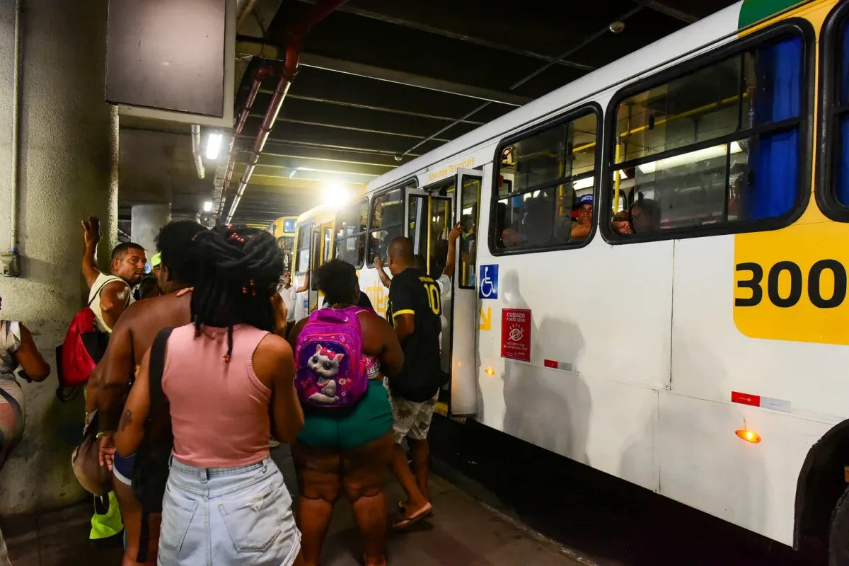 Pessoas no ponto de ônibus e um ônibus arado no ponto.